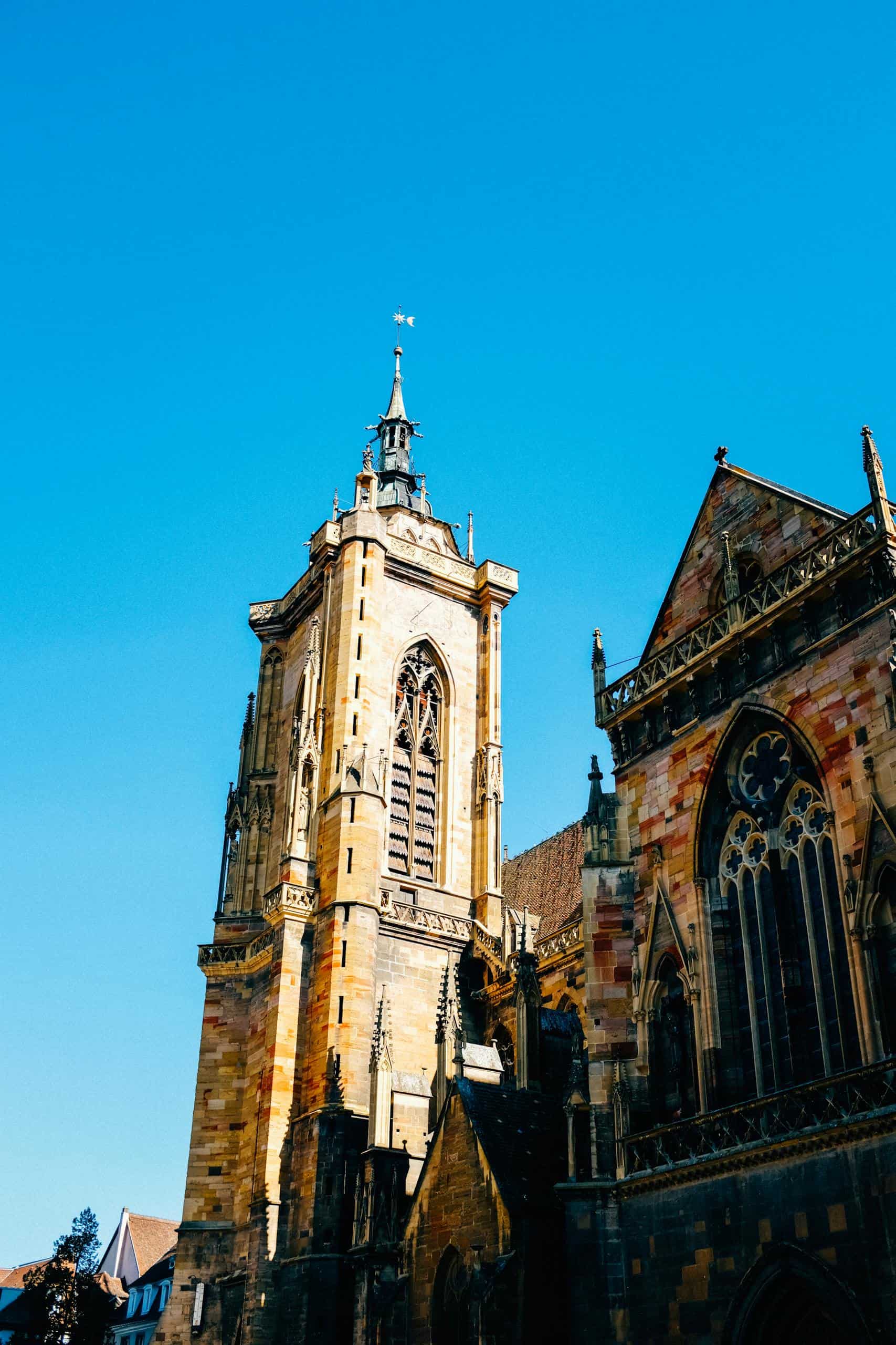 Facade of a historic Gothic cathedral in Colmar, France, with a clear blue sky.