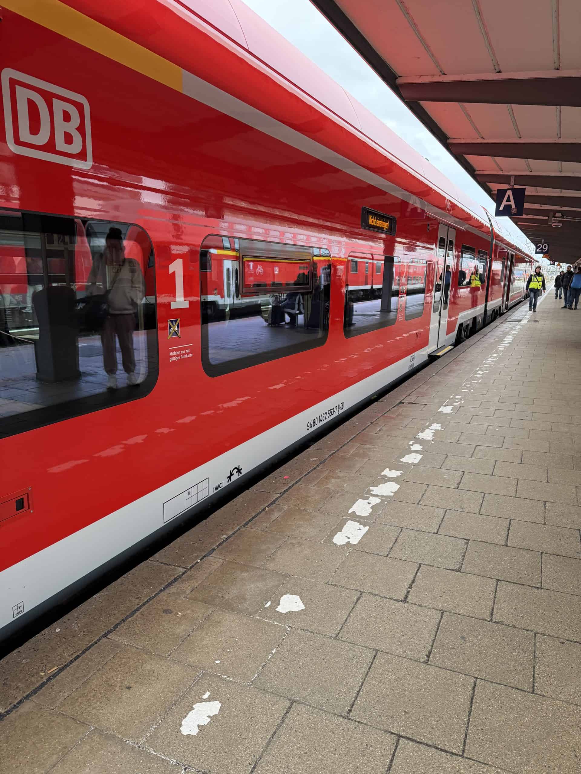 Modern red Deutsche Bahn train at a busy train station platform.