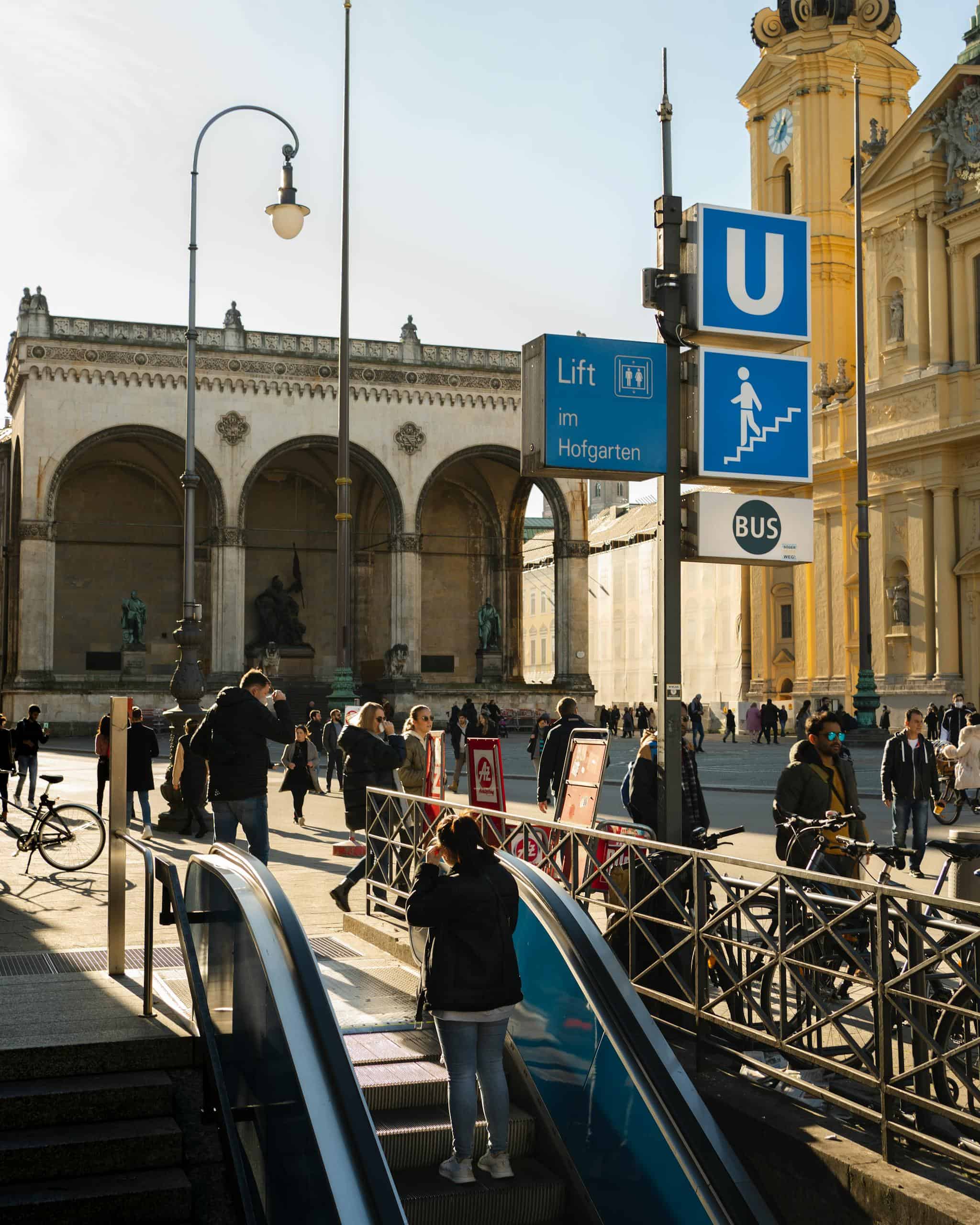Bustling Odeonsplatz in Munich with people and subway entrance, highlighting iconic landmarks.