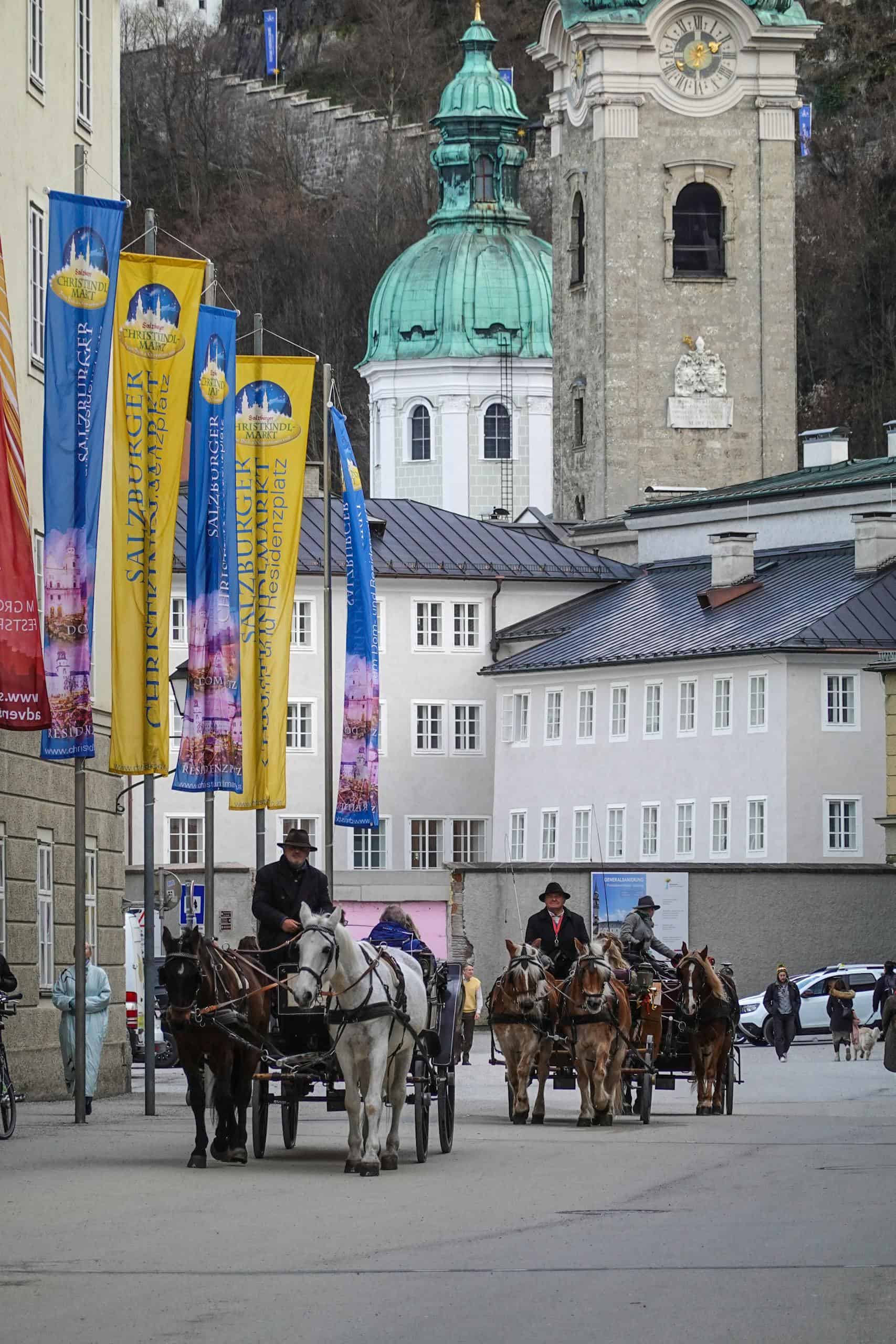 Horse-drawn carriages on a street in historic Salzburg, Austria, showcasing classic European architecture.