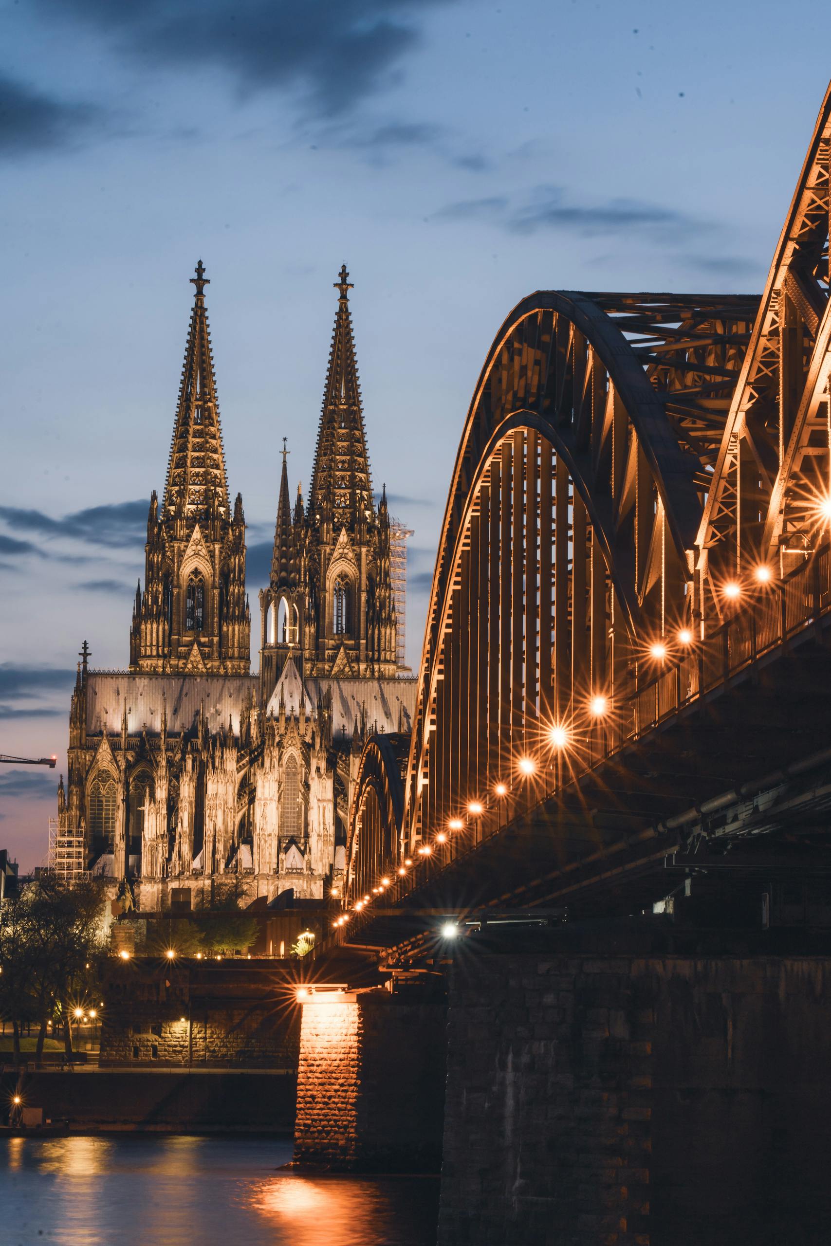 A stunning view of Cologne Cathedral and Hohenzollern Bridge illuminated during the evening in Cologne, Germany.