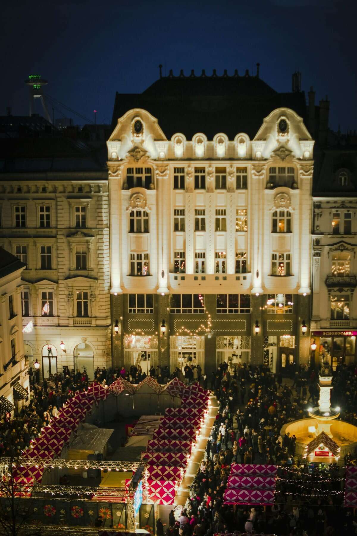 A vibrant view of Bratislava's Christmas market with festive lights and bustling crowds at night.