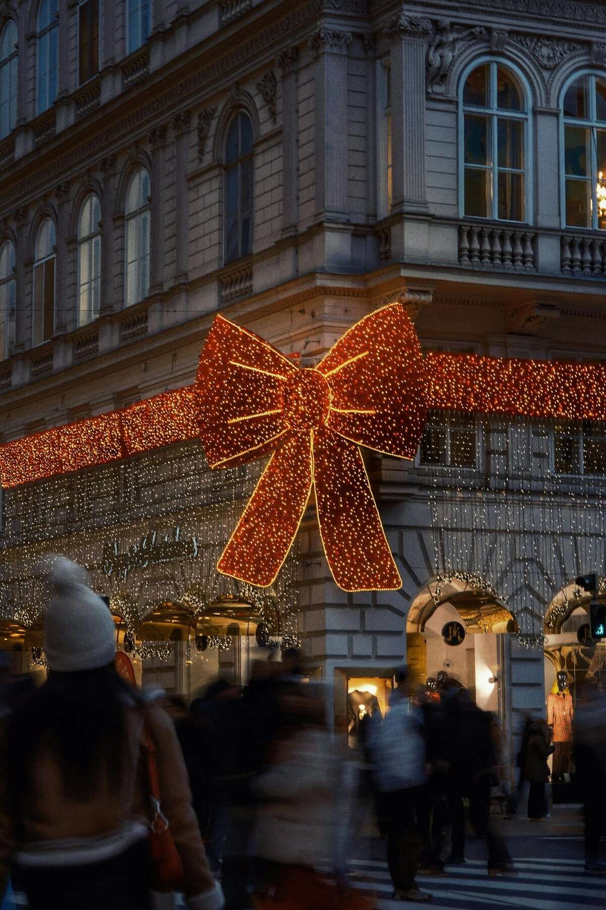 Christmas lights decorate a Vienna street with a large bow and bustling pedestrian activity.