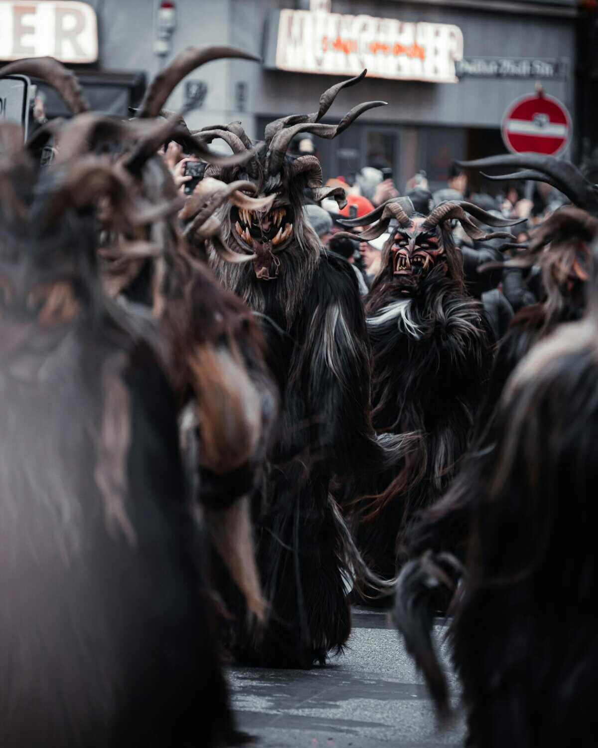 A Krampus parade featuring people in traditional costumes with horns and masks in a city street.