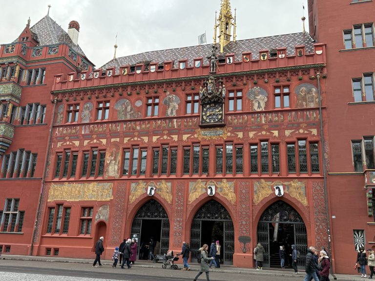 Exterior of Basel Town Hall with red façade, painted murals, and people entering during the Christmas season in Switzerland