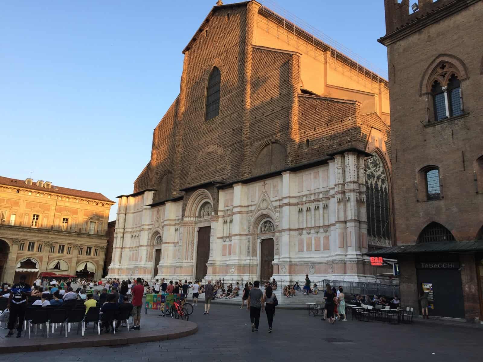 Basilica di San Petronio in Piazza Maggiore, Bologna, with people gathered in the square during an outdoor event at sunset.