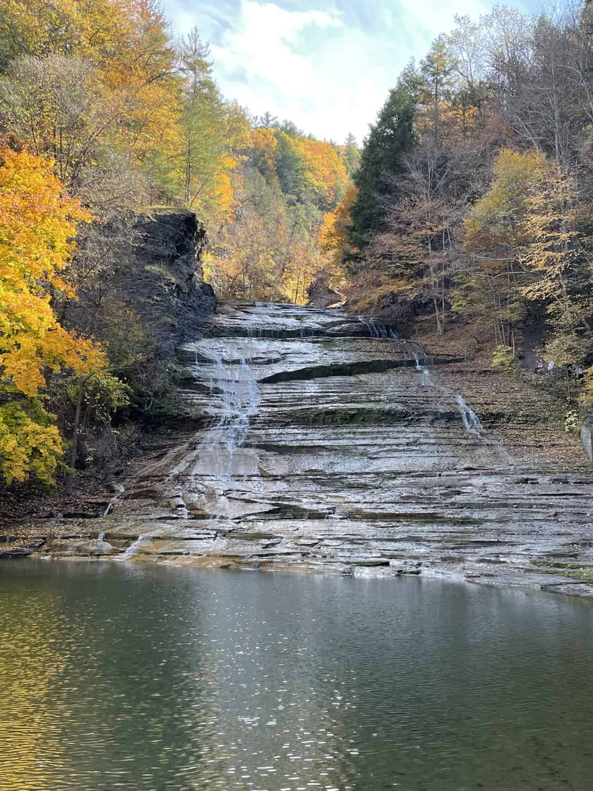 Buttermilk Falls cascading over layered rock cliffs surrounded by colorful fall foliage in Ithaca, New York