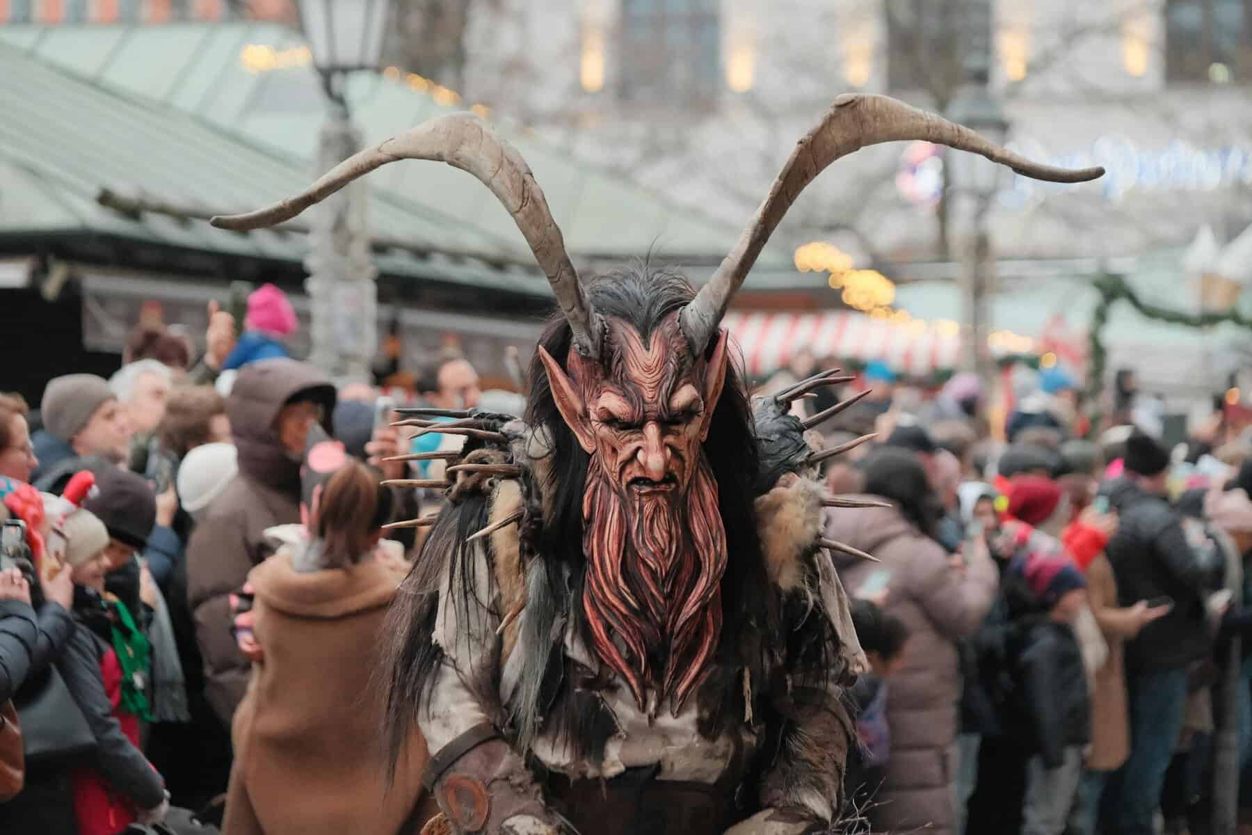 Person wearing a traditional Krampus costume with carved mask and horns at a winter festival
