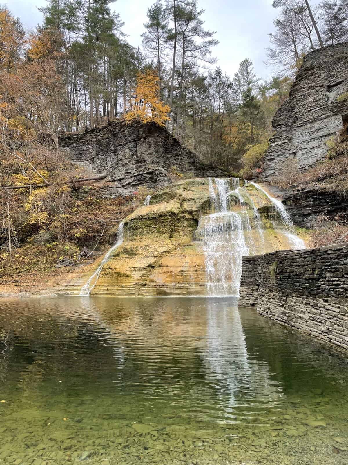 Lower Falls at Robert H. Treman State Park in Ithaca, NY cascading over layered rock ledges into a clear pool surrounded by fall foliage