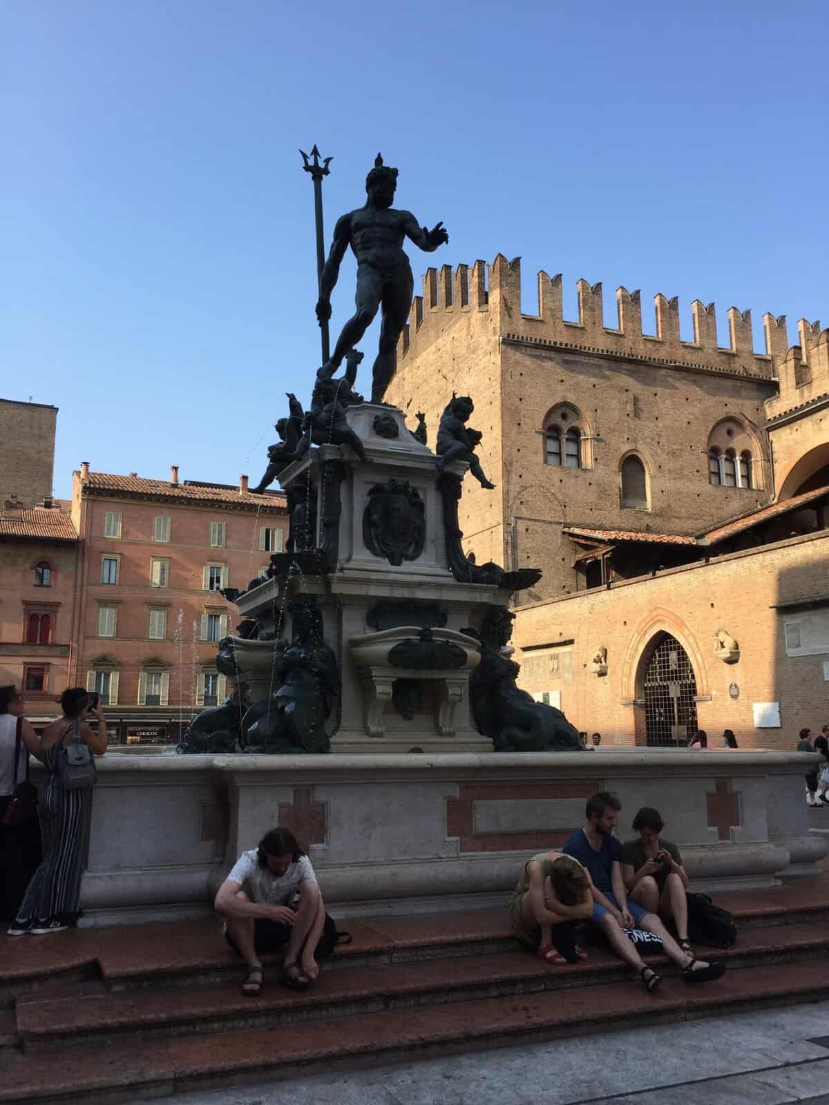 Detailed view of the Neptune fountain with tourists relaxing nearby in Bologna.