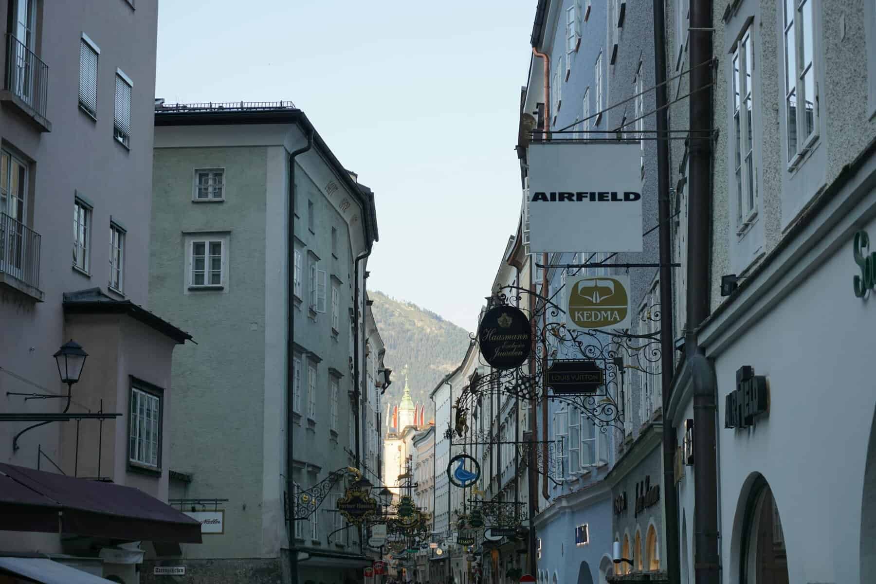 Picturesque view down a street in Salzburg, Austria featuring historic architecture and distant mountains.