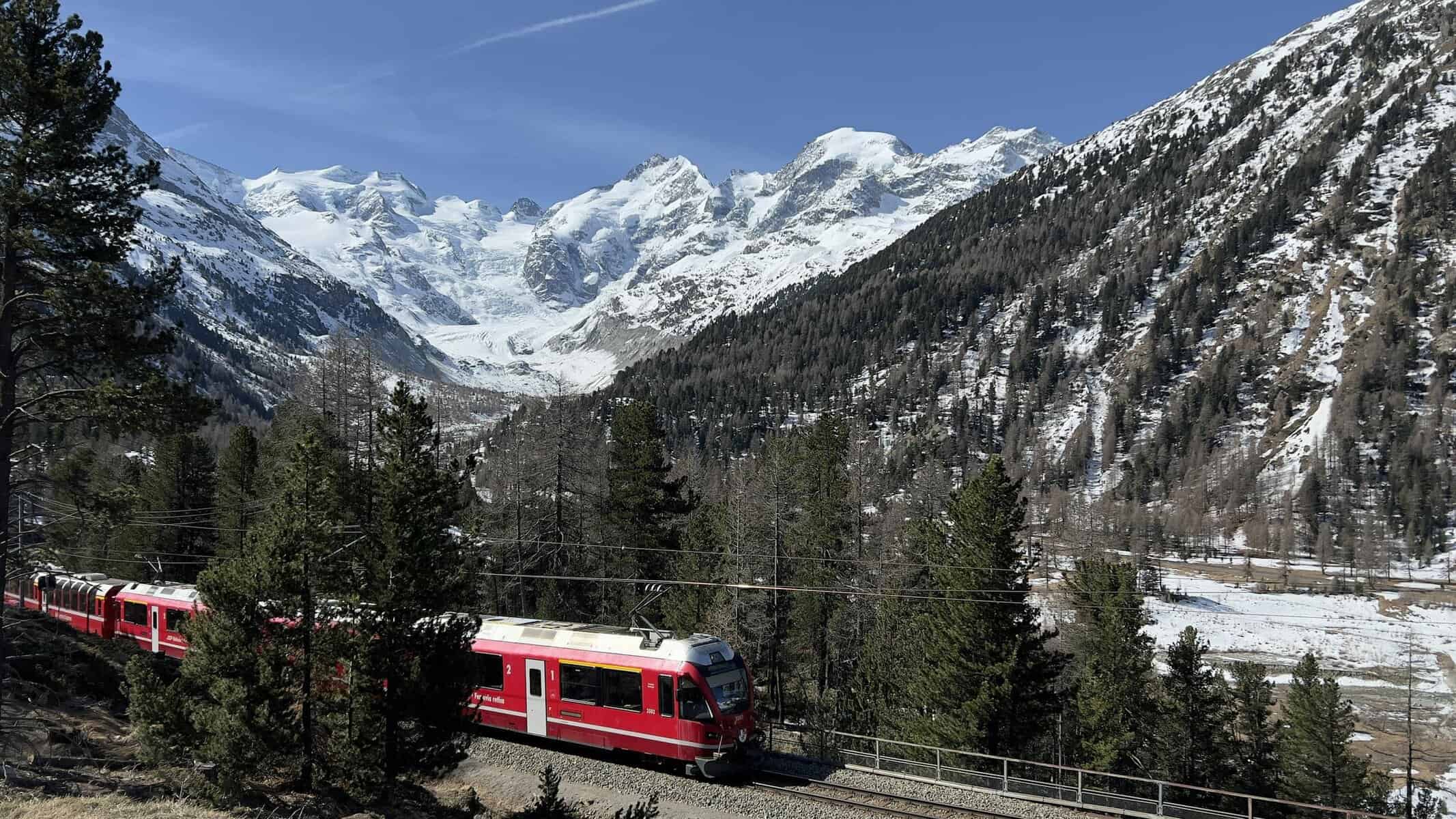 Red Bernina Express train traversing snowy Swiss Alps against a scenic backdrop.