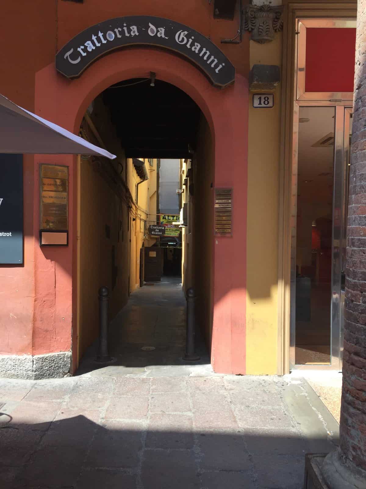 Entrance to Trattoria Gianni in Bologna, with a narrow archway leading inside beneath a traditional restaurant sign.