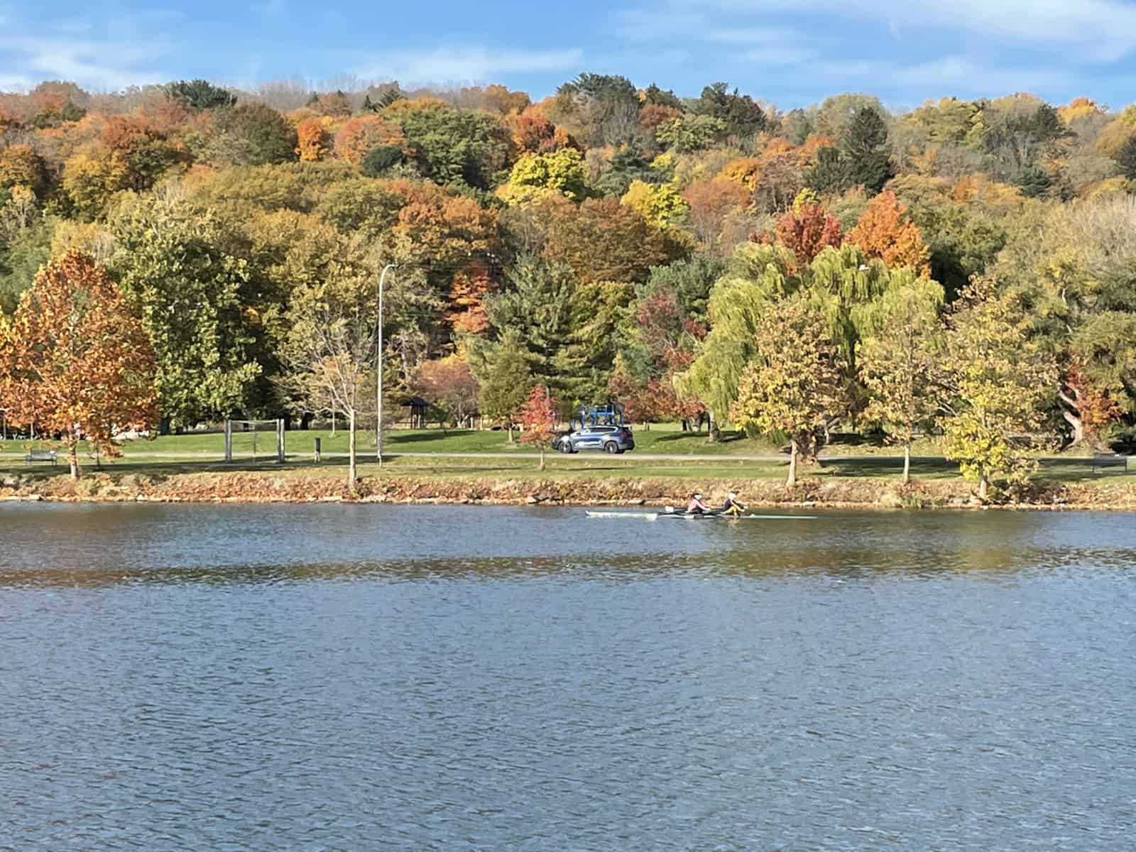 Rowers gliding across Cayuga Inlet with colorful fall foliage in Ithaca, New York