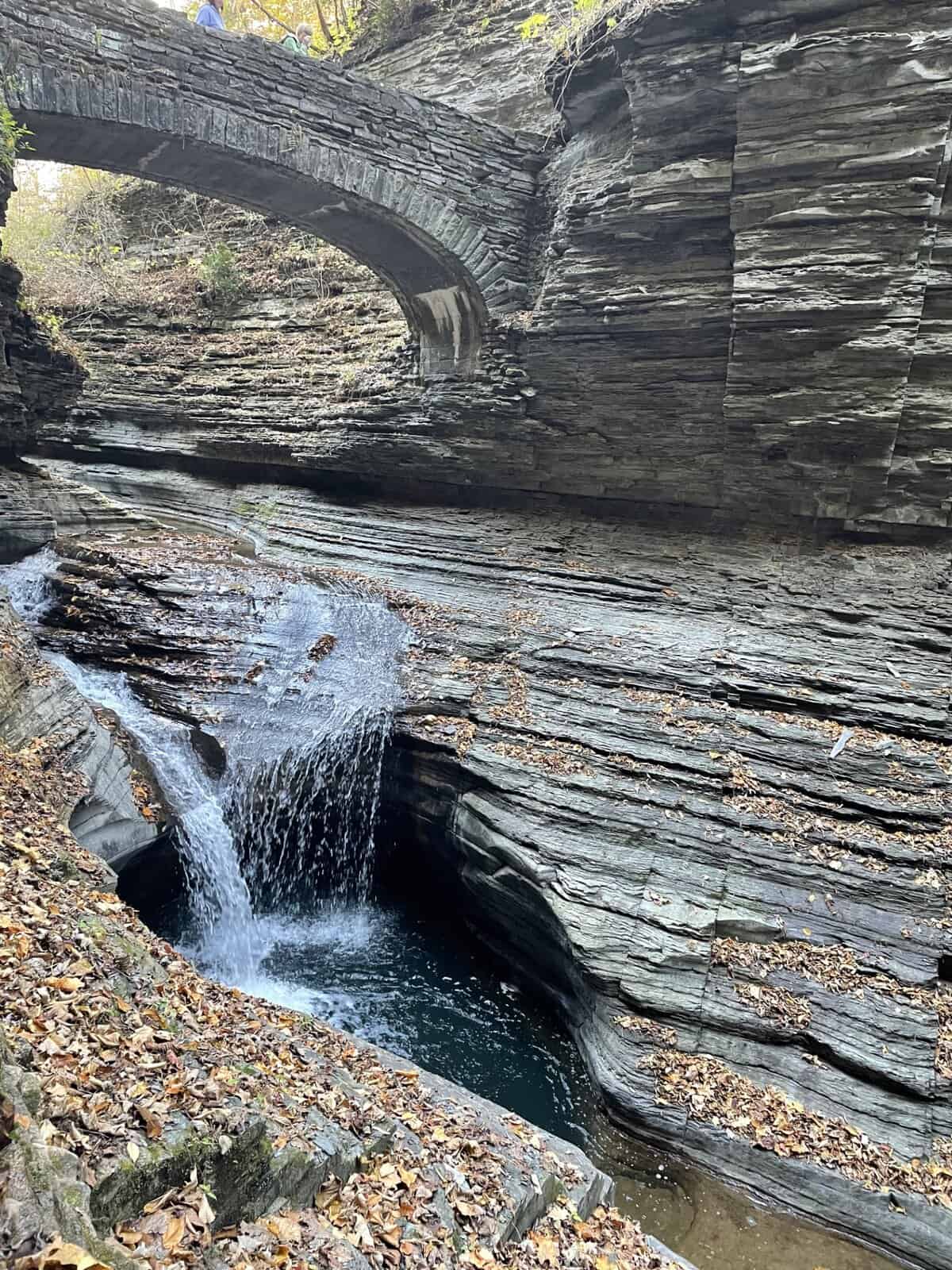 Small waterfall flowing beneath a stone bridge along the Gorge Trail at Watkins Glen State Park in New York with layered rock walls