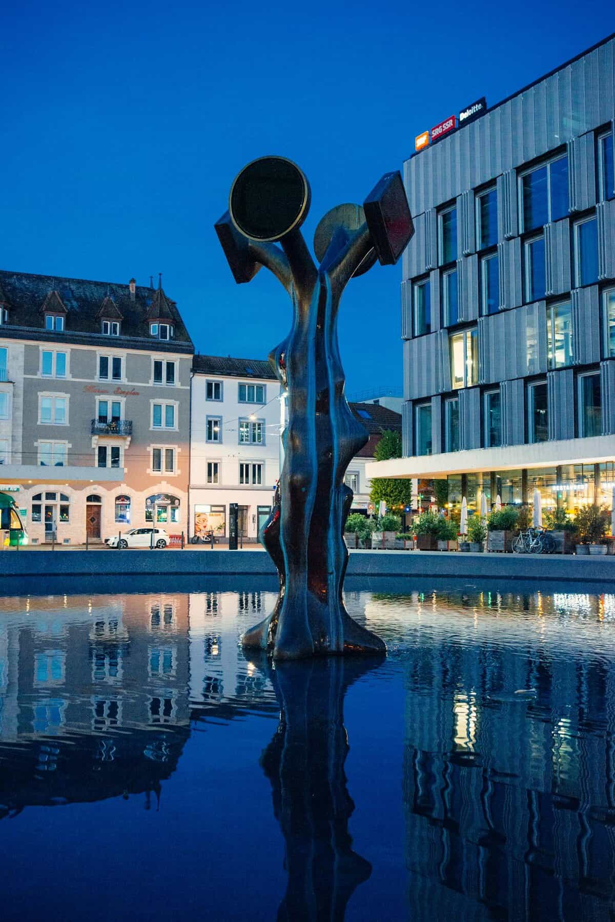 A striking modern sculpture reflecting in a water feature at twilight in Basel, Switzerland.