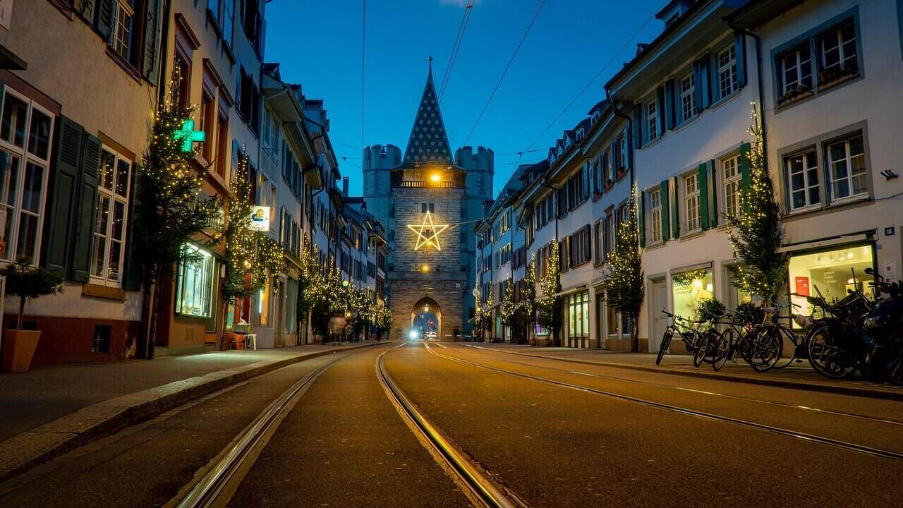 Spalentor gate in Basel at night with Christmas lights, glowing star decoration, and tram tracks leading through the Old Town street.