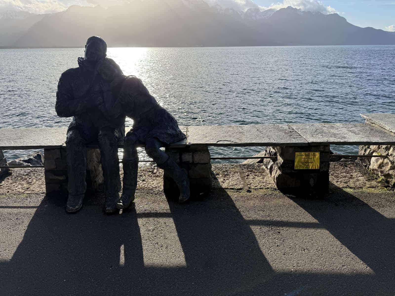 Sculpture of a couple sitting on a bench along Lake Geneva in Montreux with mountains in the background