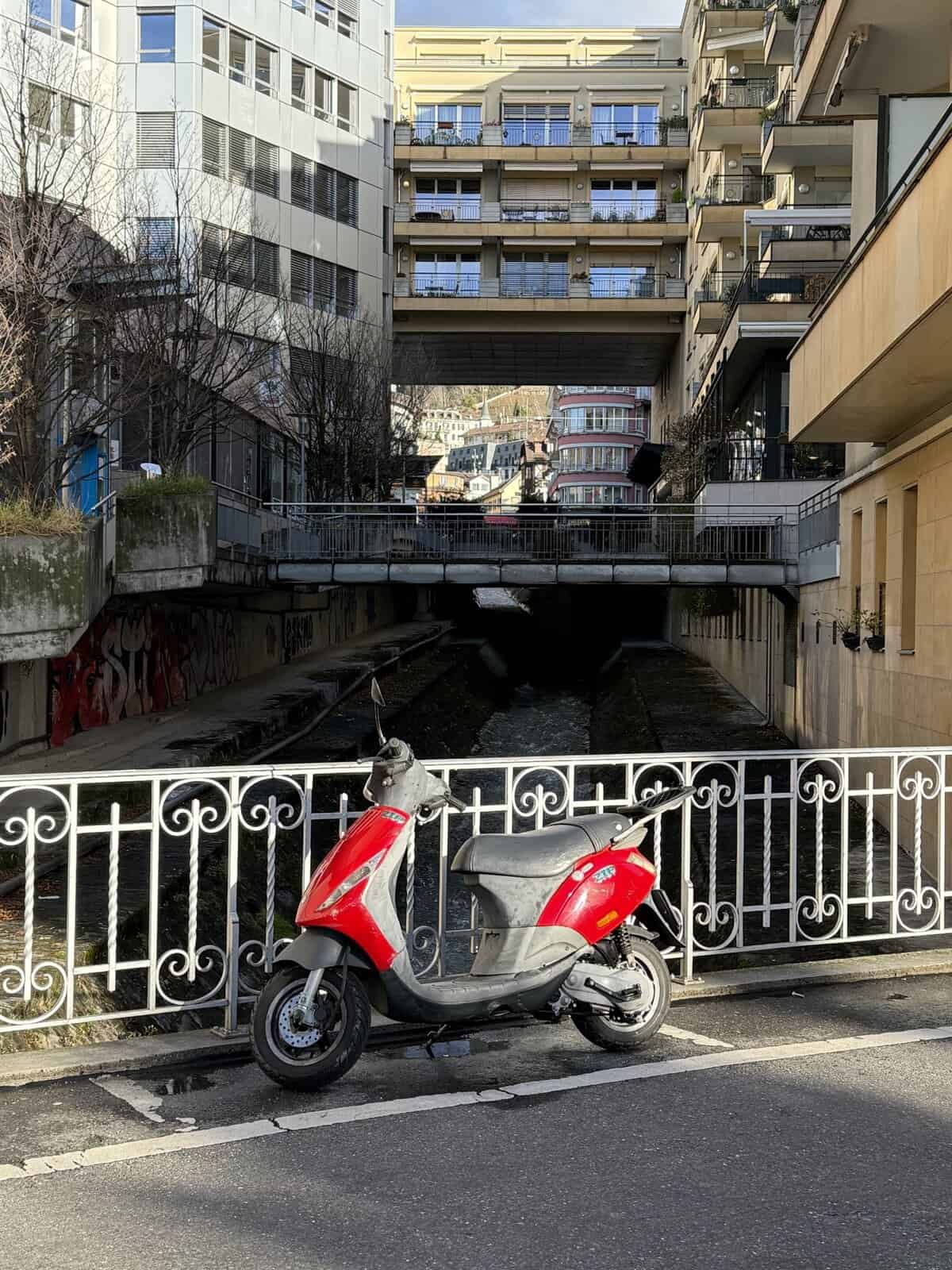 Red scooter parked along a canal in Montreux Old Town with apartment buildings above