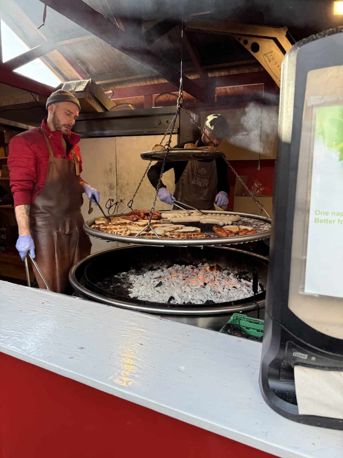 Vendors grilling sausages and cheese over open coals at the Montreux Christmas Market food stall