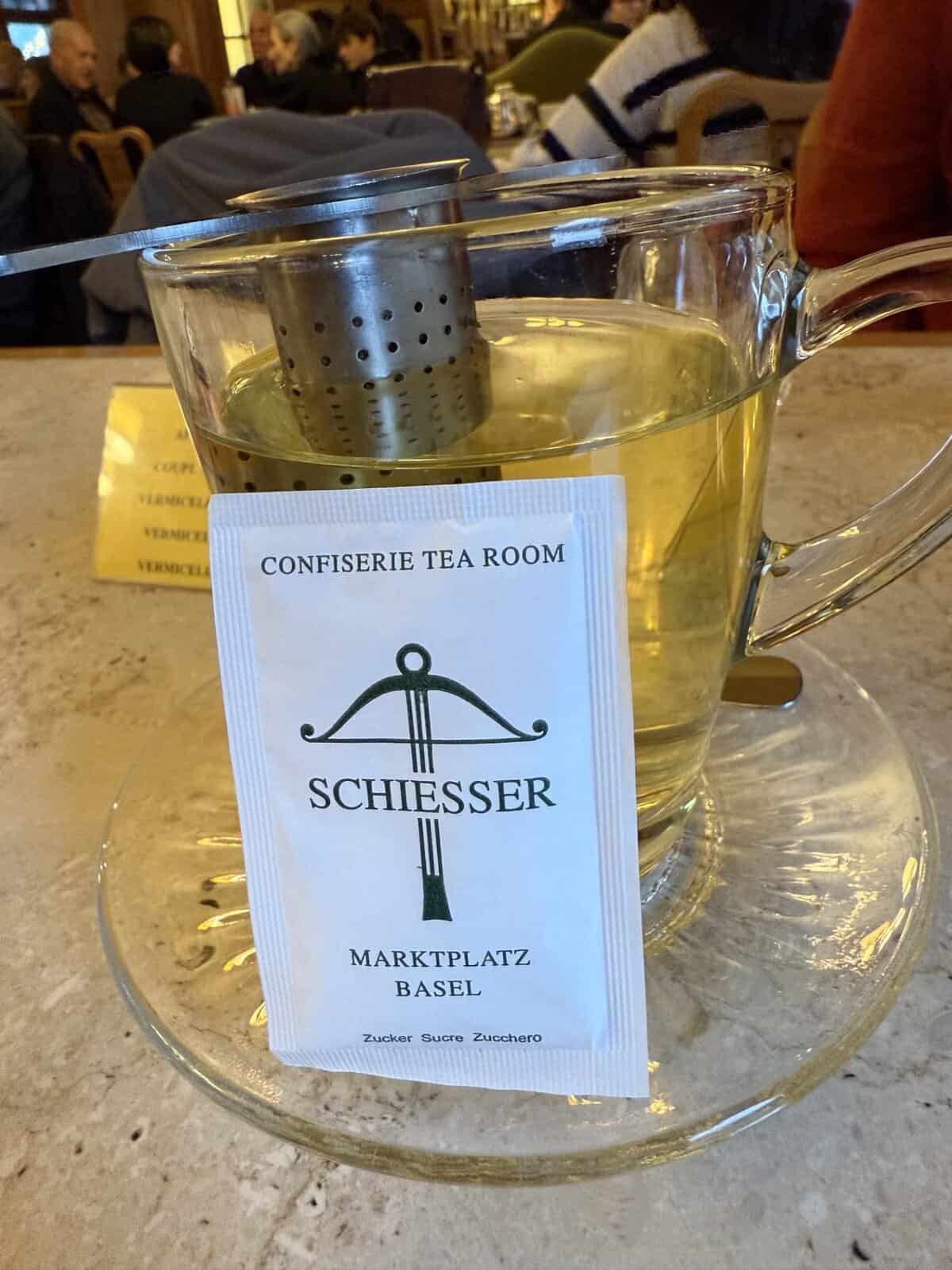 Glass cup of herbal tea at Confiserie Schiesser tea room in Basel with branded sugar packet