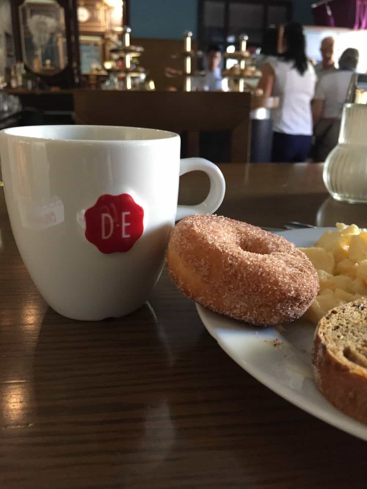 Coffee and sugar-coated donut with breakfast plate at a hotel café in Prague.