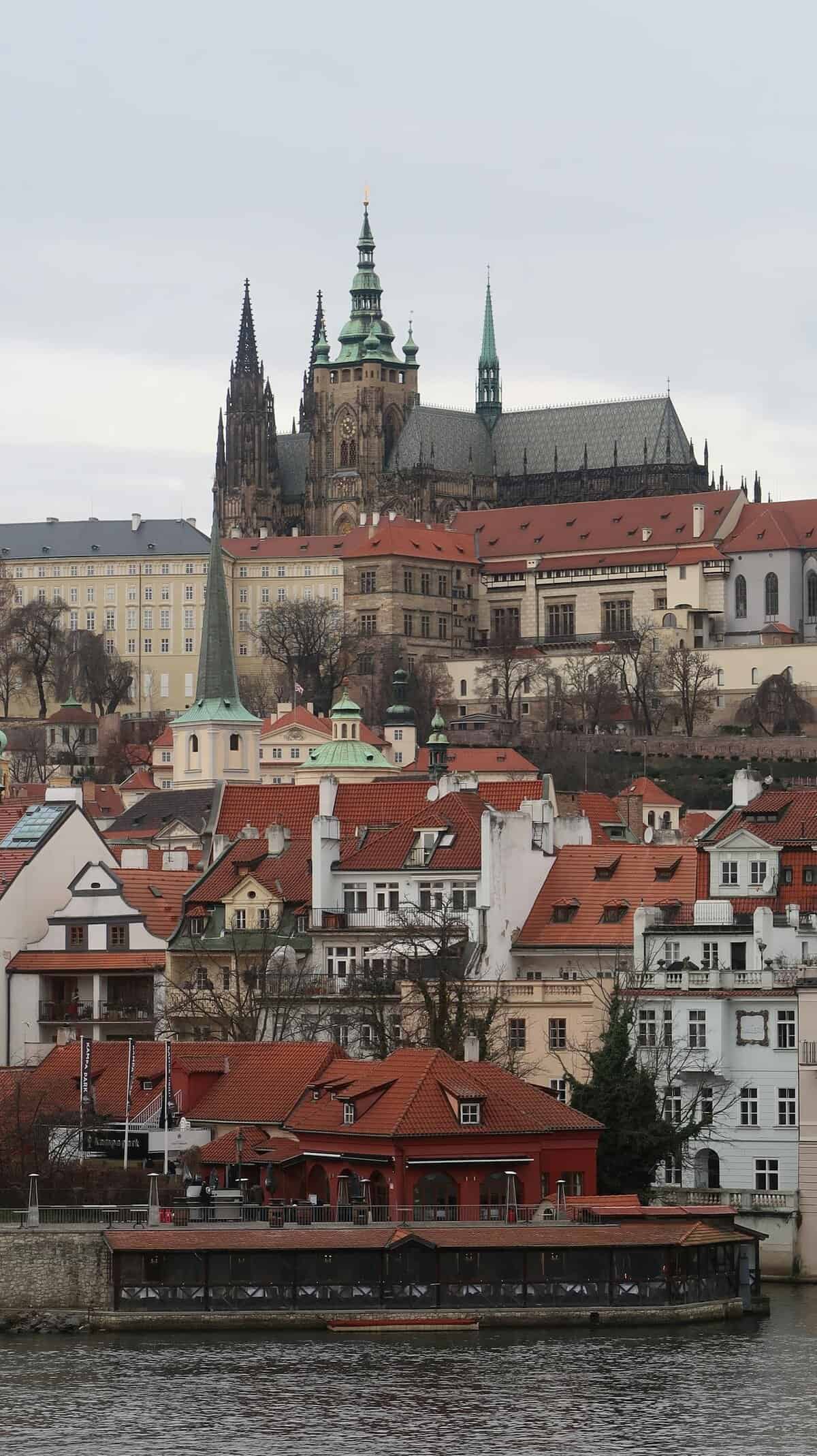 Prague Castle and charming old town buildings on a cloudy day with river view.