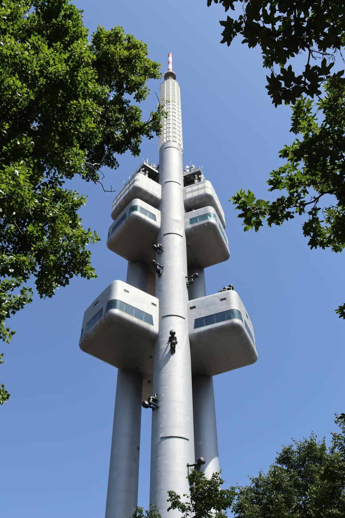 The iconic Zizkov Television Tower against a clear blue sky with surrounding trees.