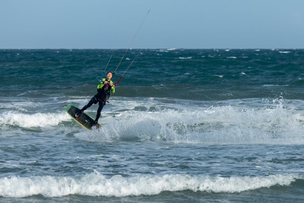 Energetic kite surfer skillfully navigating ocean waves under a clear blue sky.
