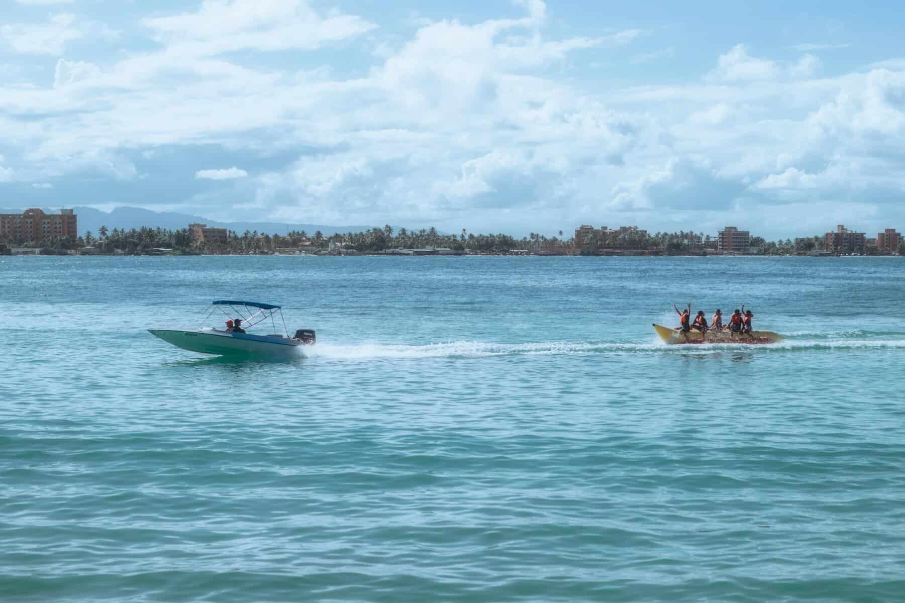Speedboat towing a banana boat on a sunny day .