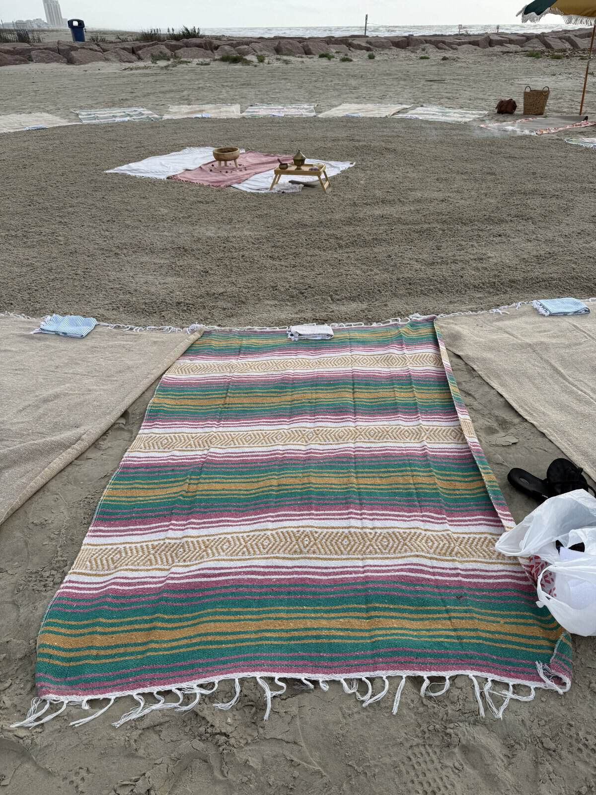 Colorful striped beach blanket spread out on the sand at a beach setup with towels, umbrellas, and the ocean in the background.