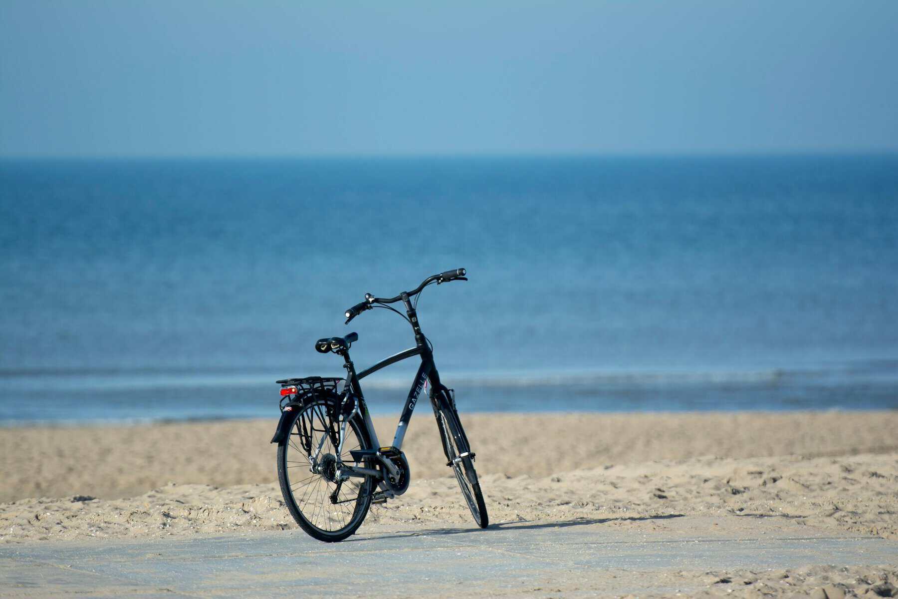A solitary bicycle rests quietly on a sandy beach overlooking serene blue waters.