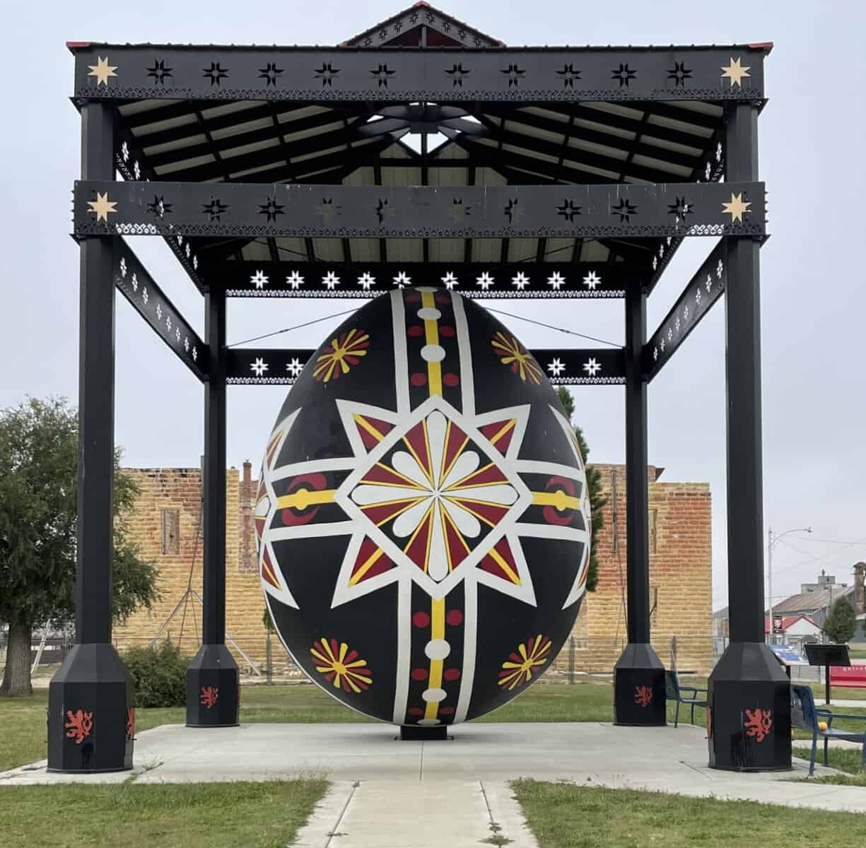 Large decorative Czech egg sculpture with traditional folk patterns displayed under a black pavilion structure outdoors.