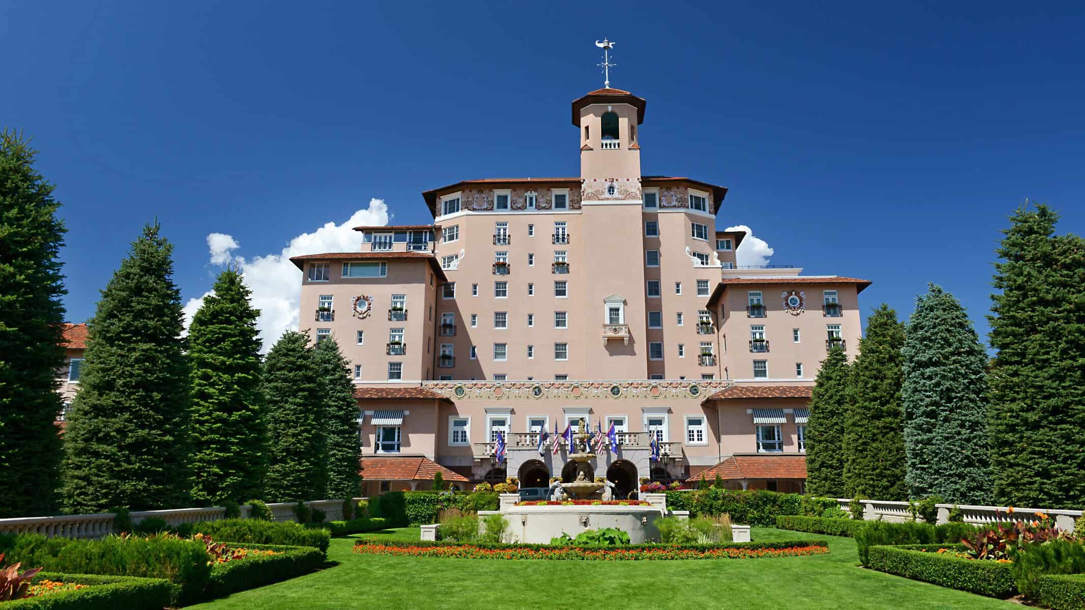 The Broadmoor luxury resort in Colorado Springs, featuring its iconic pink facade, manicured gardens, fountain, and mountain setting.