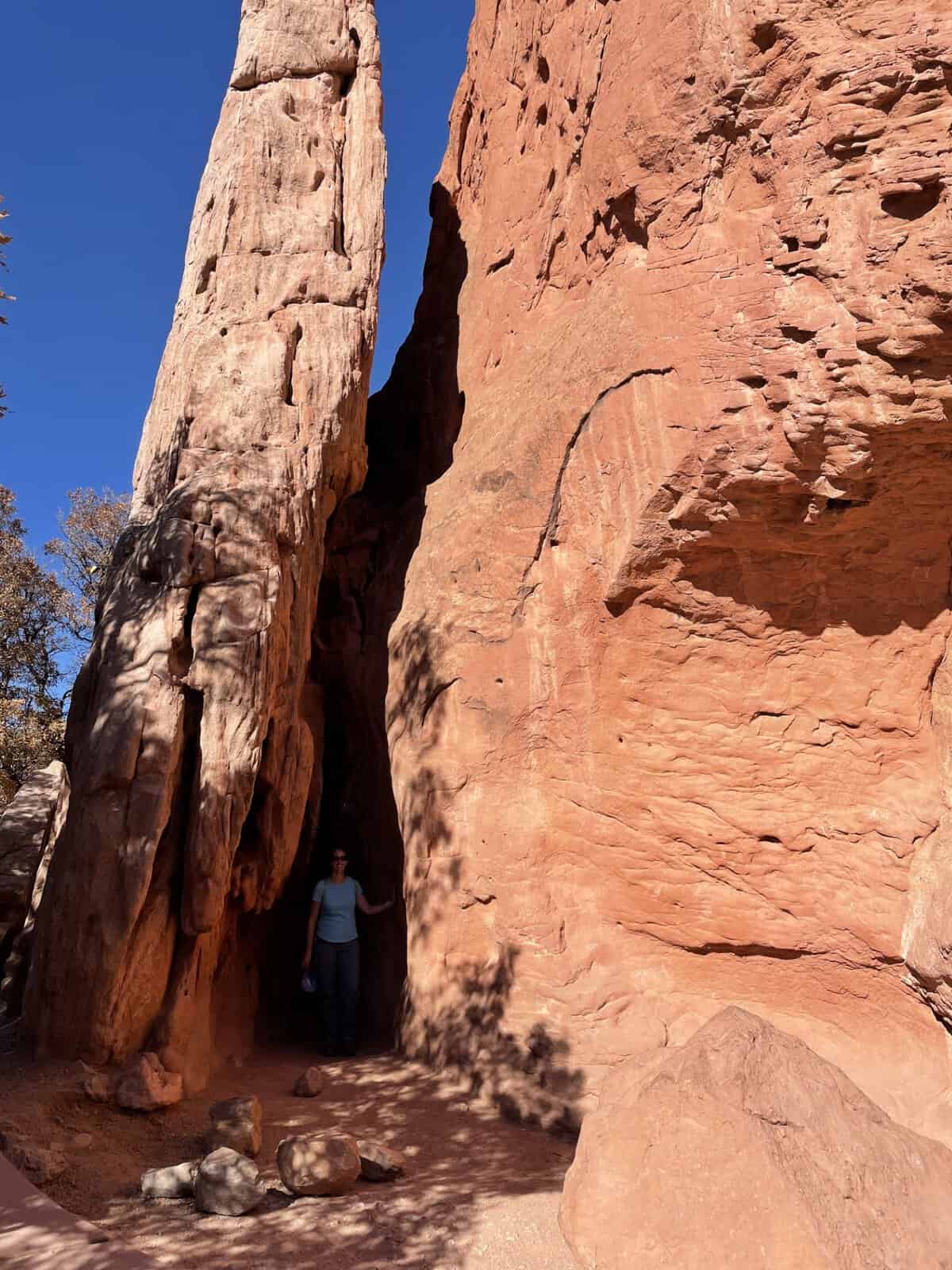 Visitor standing in the narrow passage between the towering red rock walls of the Siamese Twins formation in Garden of the Gods, Colorado Springs
