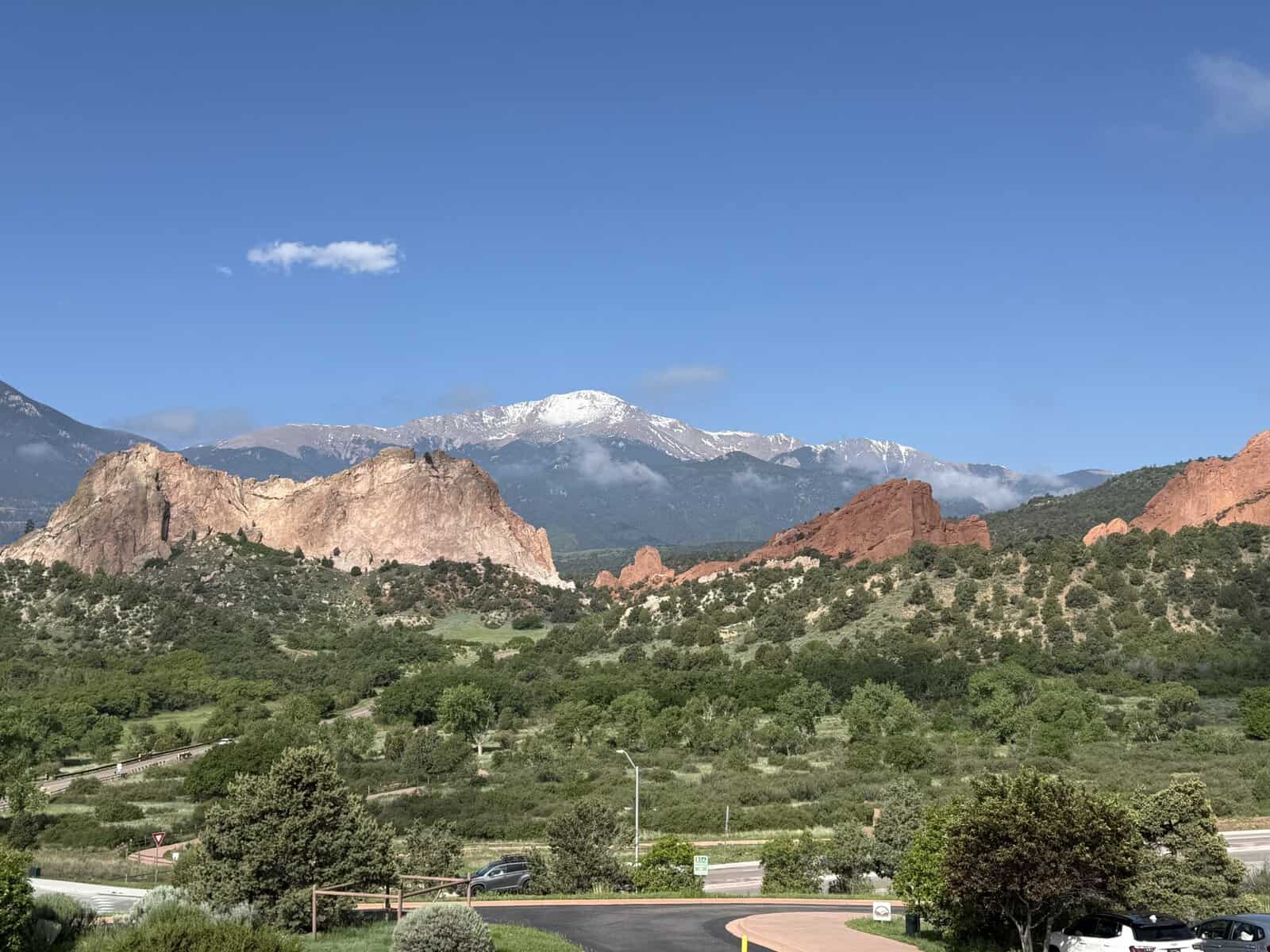View of Garden of the Gods red rock formations with snow-capped Pikes Peak in the distance under a blue sky.
