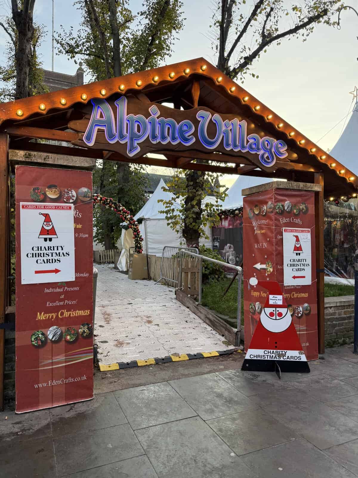Alpine Village entrance at Kingston Christmas Market with illuminated wooden archway and holiday market tents in London suburb