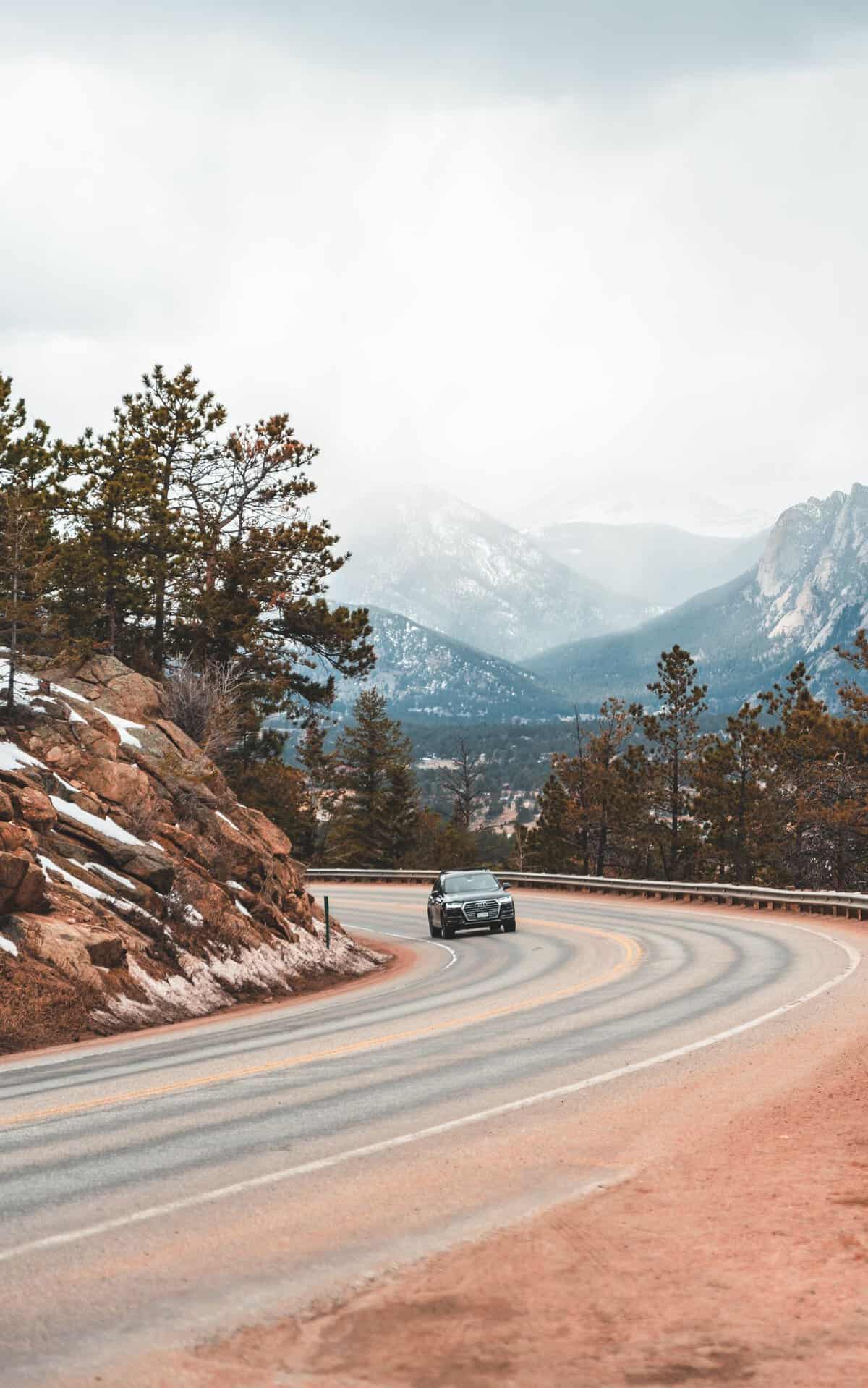Lonely black car on remote route with coniferous trees and rough snowy mountains on background
