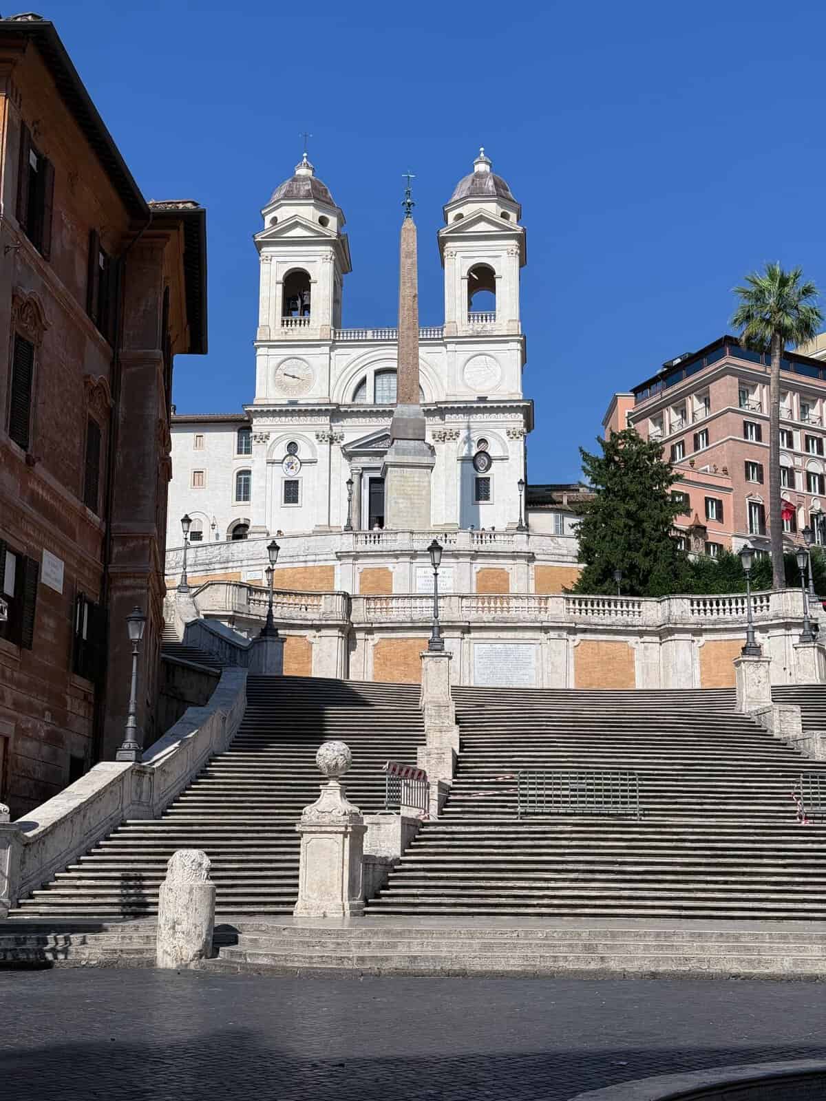 View of the renowned Spanish Steps leading to Trinità dei Monti in Rome, Italy under a clear blue sky.